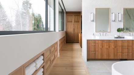 Armoires de salle de bain et parquet en bois dans une grande salle de bain blanche avec baignoire.