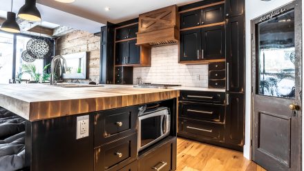 Modern dark kitchen design with central island and suspended lighting.