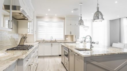 White kitchen with central island and suspended lighting, brick imitation backsplash.