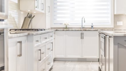 Modern white kitchen with central island and stone countertop.