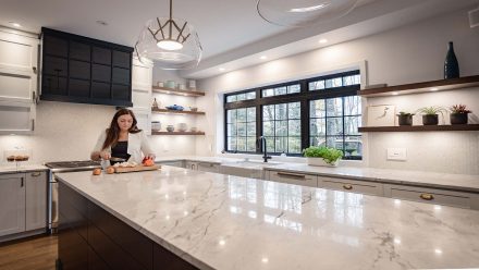 Spacious kitchen with central island, white cabinets, and natural stone countertop.