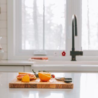 Plan cadré d'une cuisine Ateliers Jacob. Une planche à découper avec des mandarines est disposée sur le comptoir de l'îlot central. La cuisine est trés épurée et blanche.