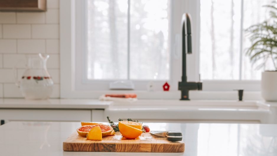 Plan cadré d'une cuisine Ateliers Jacob. Une planche à découper avec des mandarines est disposée sur le comptoir de l'îlot central. La cuisine est trés épurée et blanche.