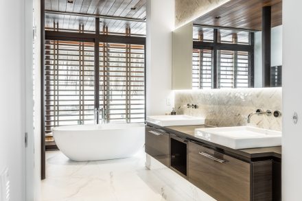 Salle de bain blanche et bois sombre, baignoire et comptoirs épurés dans une résidence à Tremblant.