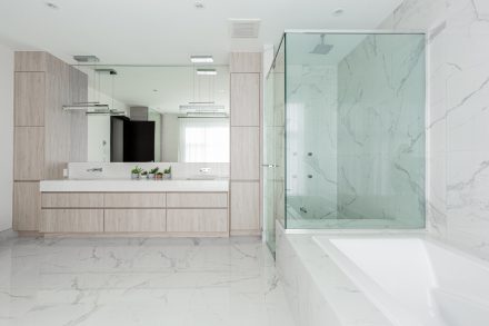 Meubles de salle de bain moderne avec armoires claires et douche en verre.