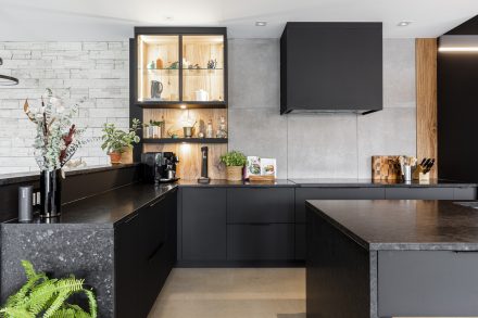 Dark industrial Kitchen with black central island and suspended cabinets on a brick wall.