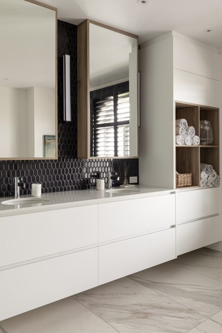 Salle de bain avec armoires blanches Ateliers Jacob et un mur en mosaic noire