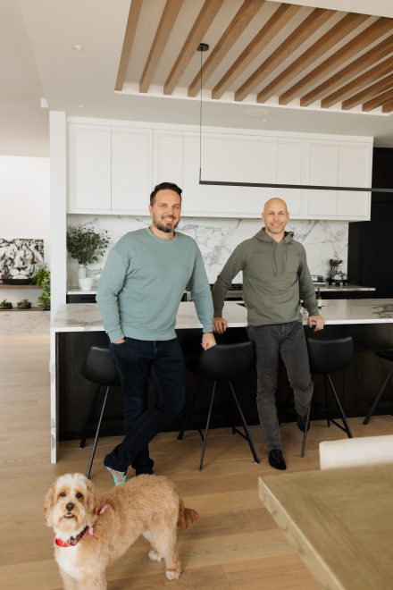 Simon Bouchard, Steve Bégin , joueur de hockey professionnel , et son chien dans sa cuisine conçue par Ateliers Jacob avec des armoires blanches en bois et un grand îlot central.