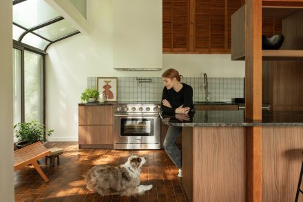 Cuisine sur mesure signée Ateliers Jacob dans la maison de Béatrice Martin (Cœur de Pirate), avec armoires en Laminé européen effet bois naturel, plancher en brique et grandes fenêtres dans l’esprit Mid-Century moderne.