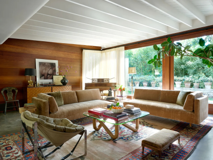 Salon lumineux dans la maison Mid-Century Modern de Dakota Johnson, avec poutres apparentes blanches et vue sur le jardin.