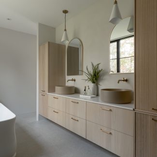 Salle de bain avec vanité Ateliers Jacob en chêne cannelé, double vasque ronde, robinetterie en laiton brossé et rangements fonctionnels.