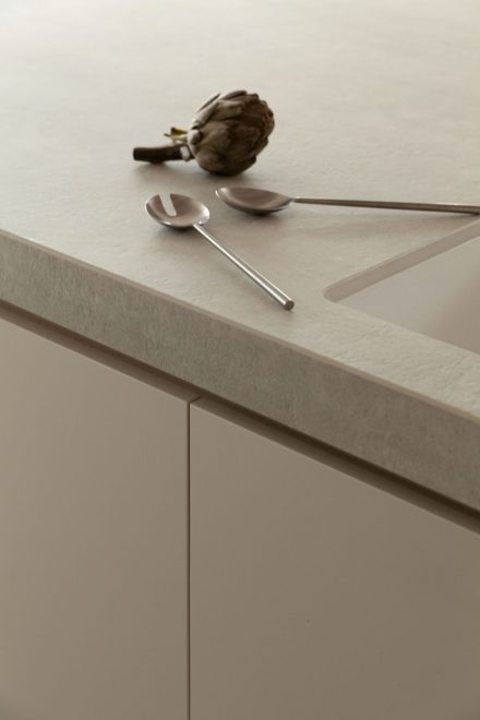 Détail de comptoir en surface Laminam dans une cuisine moderne Ateliers Jacob, avec ustensiles en acier inoxydable et artichaut posé près de l’évier intégré.