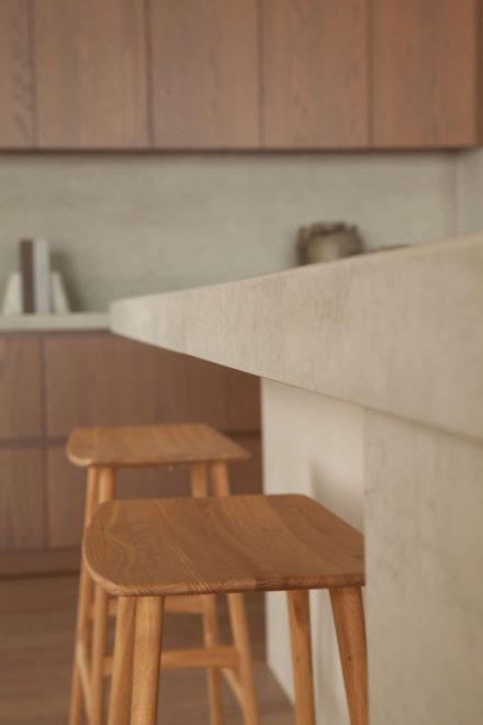 Détail de l’îlot en porcelaine Laminam dans la cuisine Farand, avec des tabourets en bois soulignant l’équilibre des matières.