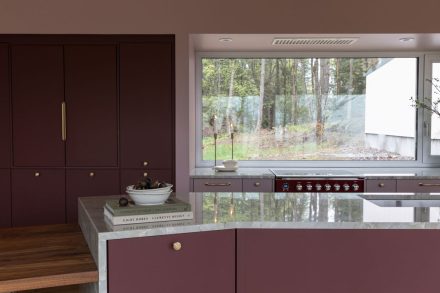 Cuisine sur mesure Ateliers Jacob avec îlot en pierre naturelle, armoires bourgogne mates, poignées en laiton