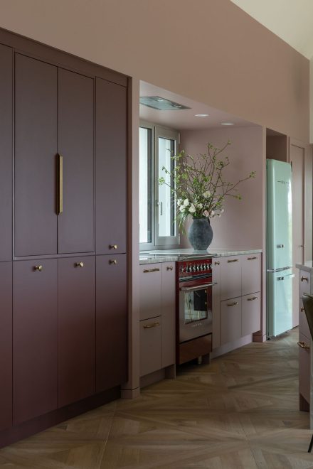 Cuisine sur mesure Ateliers Jacob avec îlot en pierre naturelle, armoires bourgogne mates, poignées en laiton avec un réfrigérateur des années 1950 turquoise