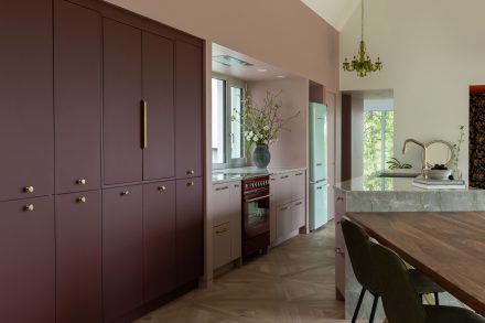 Cuisine sur mesure Ateliers Jacob avec îlot en pierre naturelle, armoires bourgogne mates, poignées en laiton