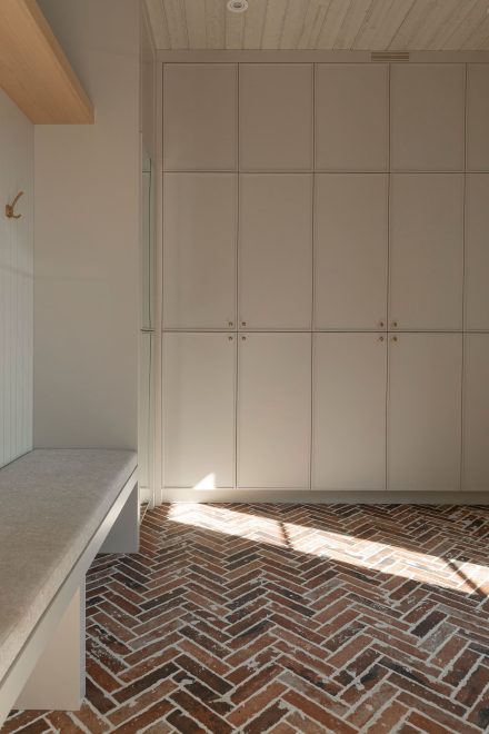 Mudroom sur mesure en bois clair avec banc intégré et tablette d’angle pour rangement de chaussures, plancher en motif chevron.