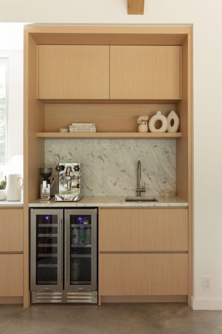 Coin barista sur mesure avec dosseret et comptoir en marbre Bianco Carrara, armoires en bois clair et celliers intégrés sous le plan de travail.