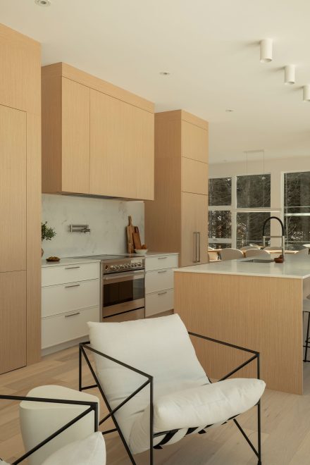 Cuisine contemporaine avec armoires en bois clair et blanches, îlot central et ouverture vers le salon, baignée de lumière naturelle.