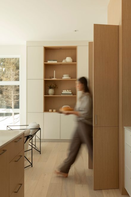 Cuisine contemporaine avec armoires en bois clair et blanches, îlot central et ouverture vers le salon, baignée de lumière naturelle.