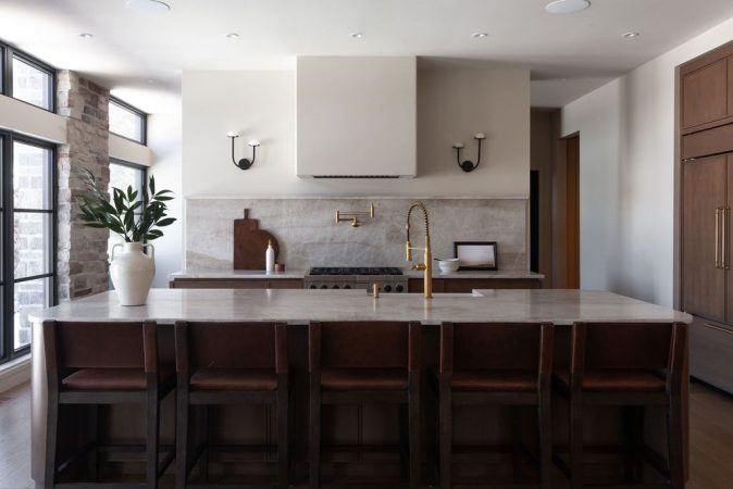 Cuisine sur mesure en chêne conçue par Ateliers Jacob au Québec, avec grand îlot central en pierre naturelle, robinetterie en laiton, hotte encastrée et dosseret en pierre, dans un aménagement lumineux aux lignes épurées.