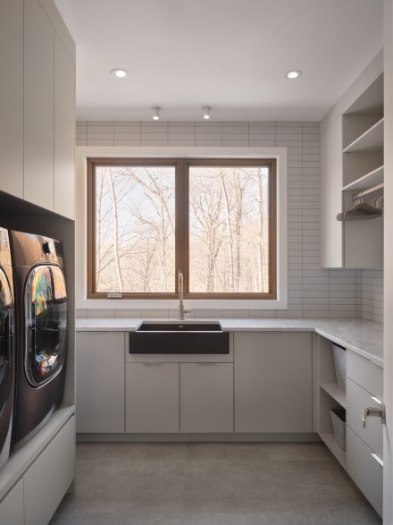Salle de lavage sur mesure avec armoires Grisaille, comptoir de quartz fini honed et fenêtre centrale apportant lumière naturelle, projet Ateliers Jacob.