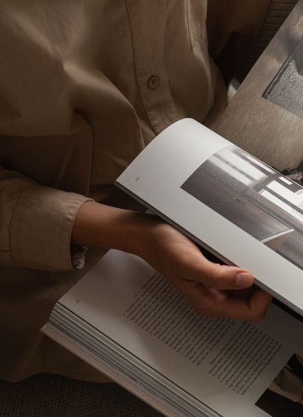 Personne feuilletant le livre Soft Minimal de Norm Architects, assise dans un fauteuil, lumière douce et ambiance chaleureuse.