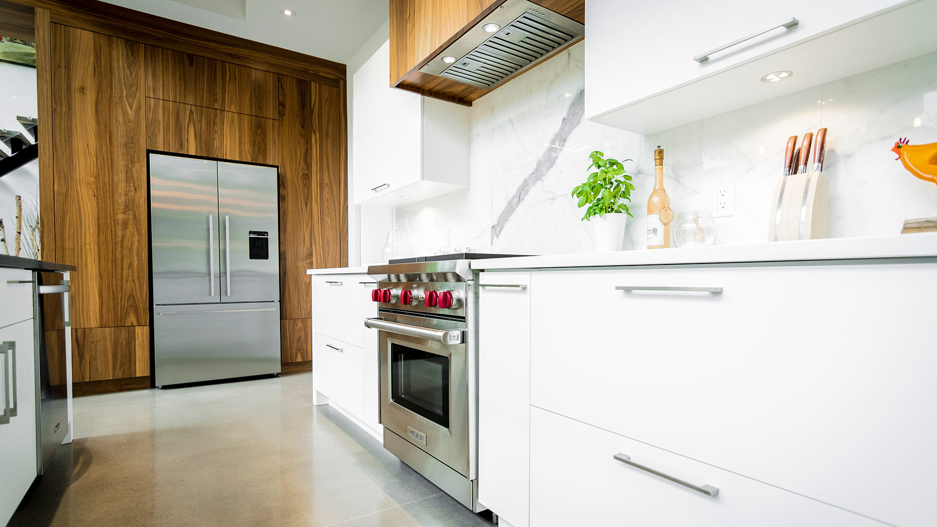 Cuisine moderne à aire ouverte. De très hautes et larges armoires de cuisine encadrent le frigo sans poignées extérieures.