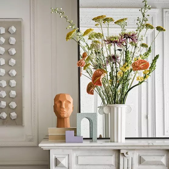 Quelques objets de décoration de style design ornementent une chemignée en marbre, en plus d'un vase contenant des fleurs.