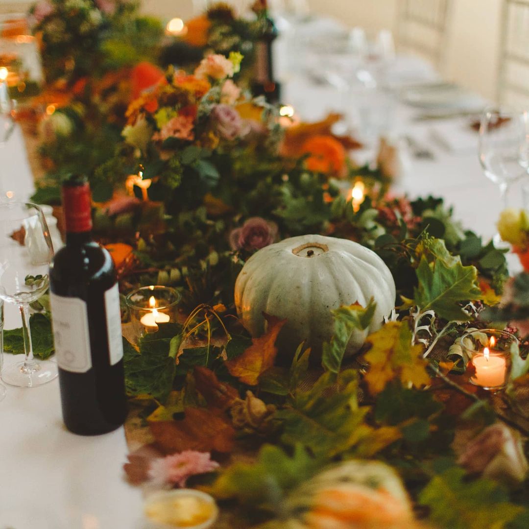 Chemin de table avec des feuilles et des petites citrouilles vertes et oranges.