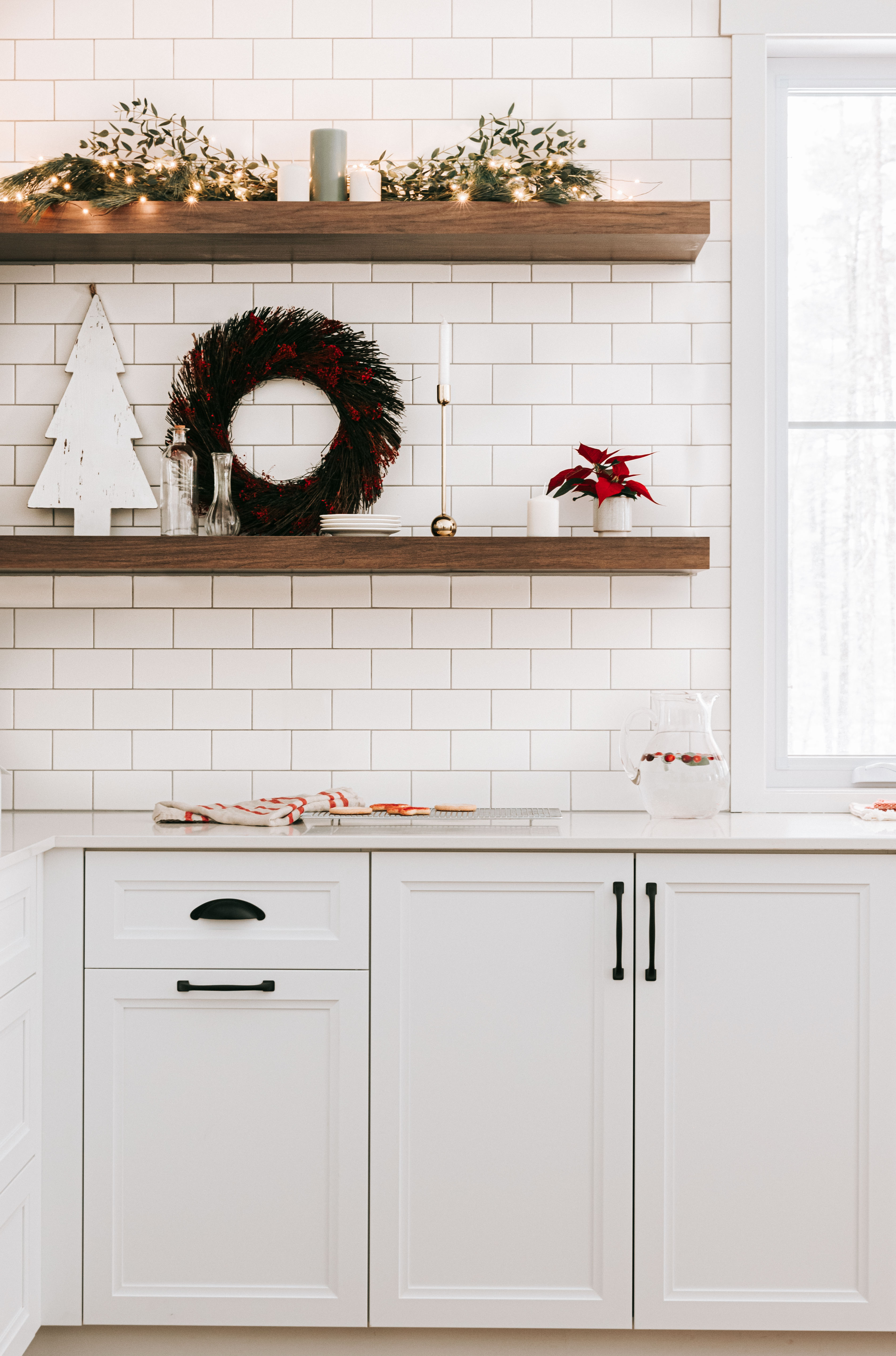 Étagères de cuisine décorées avec quelques guirlandes lumineuses, une couronne et d'autres éléments décoratifs comme des bougies.